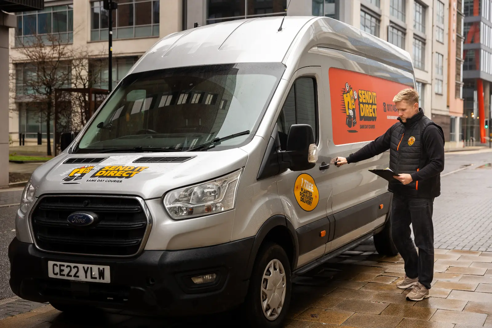 UK courier using a tablet with live delivery tracking beside a delivery van